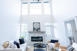 Vaulted ceiling with transom windows, white brick fireplace with a wood mantel, glass-paneled entry door, and wood-finish flooring - 