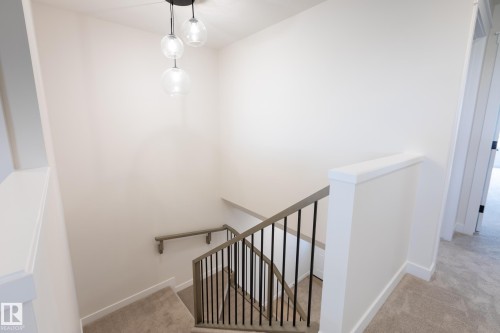 Carpeted staircase with metal balusters, wood-finish handrails, and a contemporary multi-globe pendant light fixture - 6306 65 Ave, Beaumont, AB 