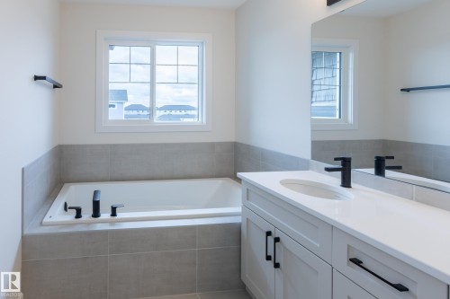 Built-in tub with matte black fixtures, framed window, and a tile surround - 6306 65 Ave, Beaumont, AB 
