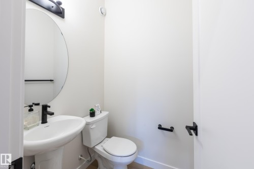 Pedestal sink with a matte black faucet, wall-mounted oval mirror, and contemporary black vanity light - 6306 65 Ave, Beaumont, AB 