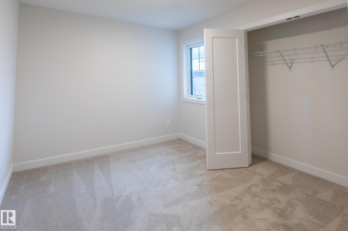 Light-colored carpeting, white walls, and a window with white trim, complemented by a white solid panel door and a closet with a wire shelving system - 6306 65 Ave, Beaumont, AB 