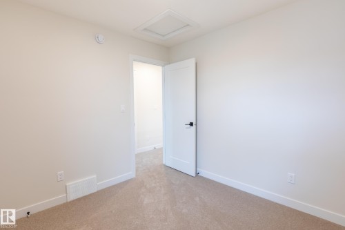 Neutral-toned carpet flooring, white walls, and a white interior door with matte black hardware - 6306 65 Ave, Beaumont, AB 