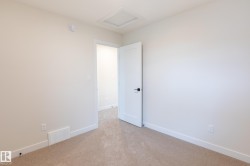 Neutral-toned carpet flooring, white walls, and a white interior door with matte black hardware - 