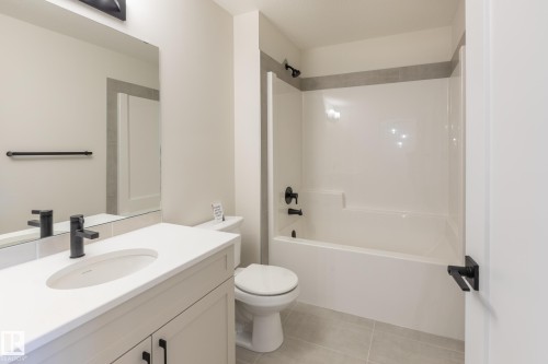 Contemporary bathroom featuring a white vanity with an integrated sink, matte black hardware, a combination shower and tub, and light-toned floor tiling - 6306 65 Ave, Beaumont, AB 