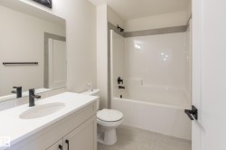 Contemporary bathroom featuring a white vanity with an integrated sink, matte black hardware, a combination shower and tub, and light-toned floor tiling - 
