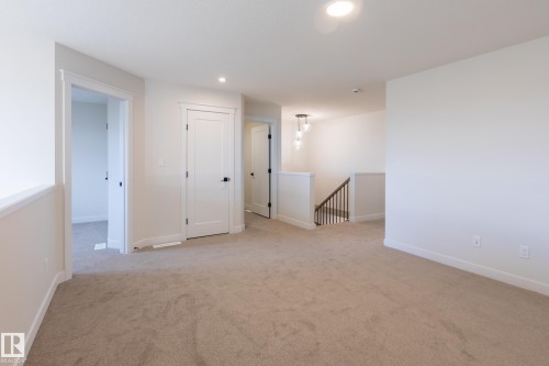 Open-concept loft area featuring neutral carpeting, recessed lighting, and a contemporary chandelier - 6306 65 Ave, Beaumont, AB 