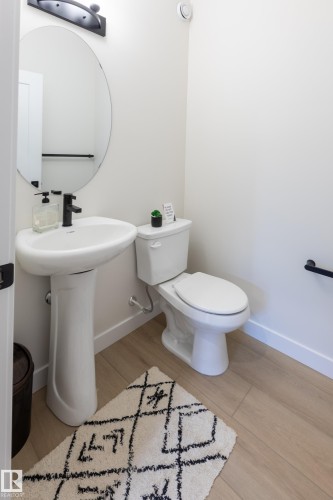 Pedestal sink with a matte black faucet, wall-mounted oval mirror, and wood-finish flooring - 6306 65 Ave, Beaumont, AB 