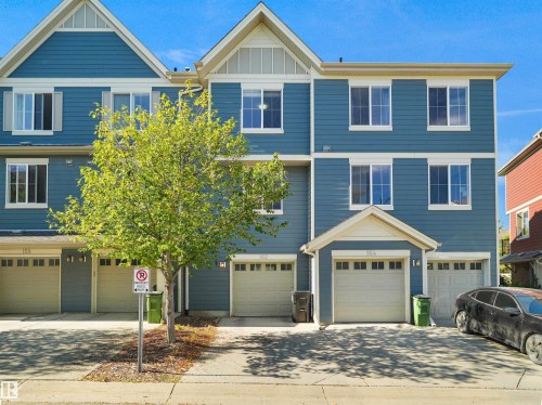 Multi-level townhome featuring blue siding, white window trim, and multiple attached garages - #162 603 Watt Bv Sw, Edmonton, AB 