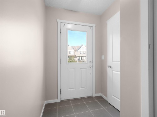 Entryway featuring a white paneled door with an integrated window, dark gray square tile flooring, and light neutral painted walls - #162 603 Watt Bv Sw, Edmonton, AB 