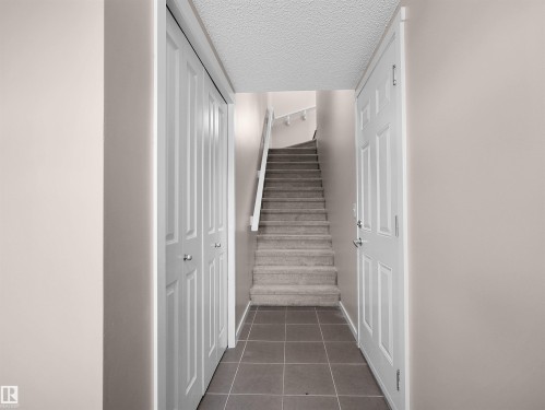 Tiled flooring, paneled interior door, bi-fold closet doors, carpeted staircase, and white handrail - #162 603 Watt Bv Sw, Edmonton, AB 