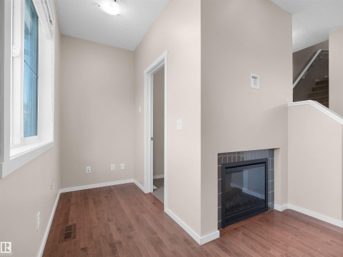 Hardwood-style flooring, a large window, a built-in fireplace with a tiled surround, and a staircase with a white handrail - #162 603 Watt Bv Sw, Edmonton, AB 