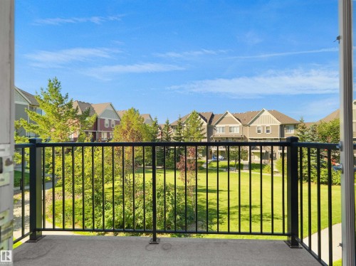 Balcony with a black metal railing and concrete flooring, overlooking a green space with mature trees - #162 603 Watt Bv Sw, Edmonton, AB 