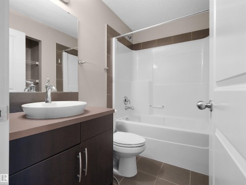 Bathroom featuring a vanity with a vessel sink, dark wood-finish cabinetry, a large wall mirror, and a white tub with shower - #162 603 Watt Bv Sw, Edmonton, AB 