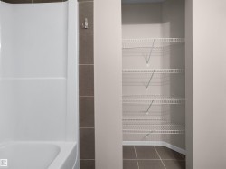 White bathtub with integrated shower, brown vertical tile accent, and a built-in closet with wire shelving and tile flooring - 