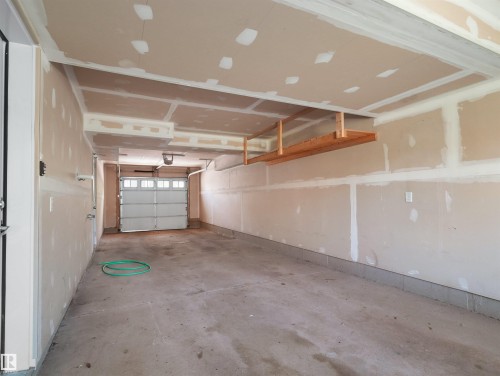 Attached garage with concrete flooring, overhead wooden shelving, and a paneled garage door - #162 603 Watt Bv Sw, Edmonton, AB 