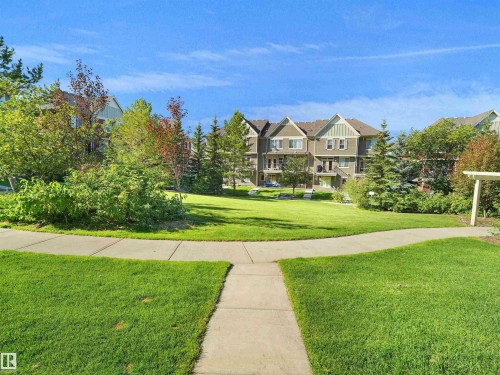 Expansive green space featuring a concrete pathway, mature trees, and shrubs - #162 603 Watt Bv Sw, Edmonton, AB 