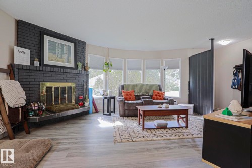 Black brick fireplace with brass-toned insert, wood-finish flooring, and a bay window - 21 Burlington Avenue, Spruce Grove, AB 