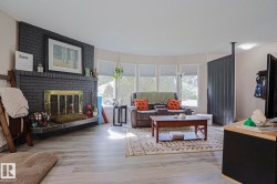Black brick fireplace with brass-toned insert, wood-finish flooring, and a bay window - 