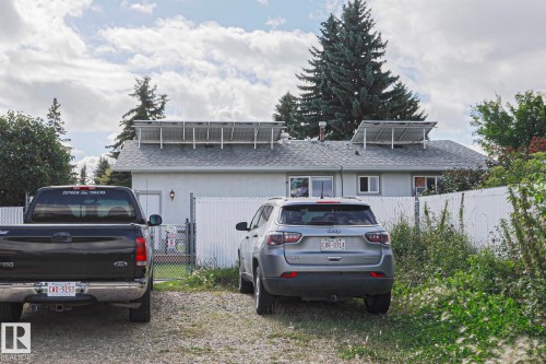 Rear exterior featuring roof-mounted solar panels, multiple windows, and chain-link fencing - 21 Burlington Avenue, Spruce Grove, AB 