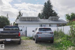 Rear exterior featuring roof-mounted solar panels, multiple windows, and chain-link fencing - 