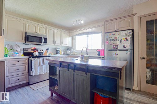 Kitchen featuring light cabinetry, stainless steel appliances, a center island with built-in storage, and wood-finish flooring - 21 Burlington Avenue, Spruce Grove, AB 