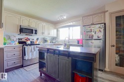 Kitchen featuring light cabinetry, stainless steel appliances, a center island with built-in storage, and wood-finish flooring - 