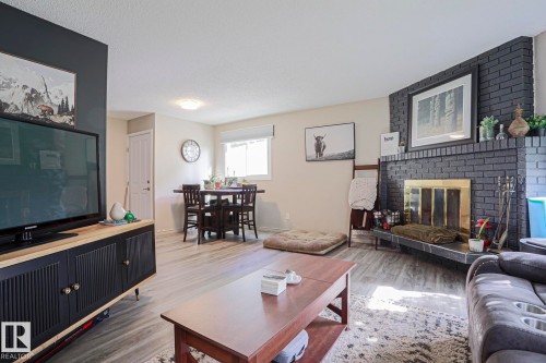 Living area with wood-finish flooring, a brick fireplace, and a dining area with a window - 21 Burlington Avenue, Spruce Grove, AB 