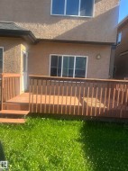 Rear exterior featuring a wood deck with railing, sliding glass doors, and a stucco finish - 