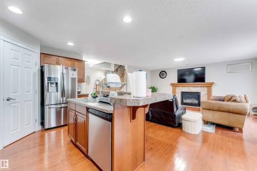Wood-finish flooring throughout, kitchen island with built-in sink and dishwasher, stainless steel appliances, and a stone-faced fireplace with wood mantel - 3012 25 Ave Avenue Nw, Edmonton, AB 