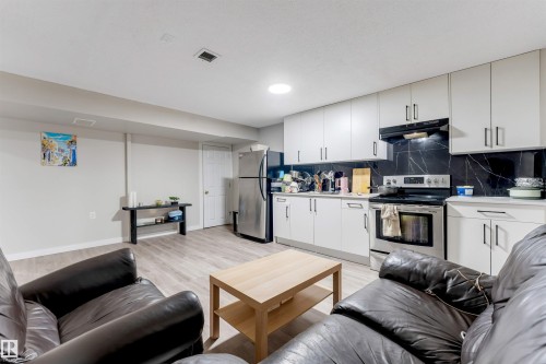 Kitchenette featuring white cabinetry, stainless steel appliances, black marble-look backsplash, and wood-finish flooring - 3012 25 Ave Avenue Nw, Edmonton, AB 