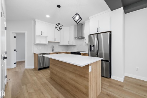 Modern kitchen featuring wood-finish flooring, white cabinetry, a large kitchen island with white countertop, and stainless steel appliances - 960 Elderberry Landing Nw, Edmonton, AB 