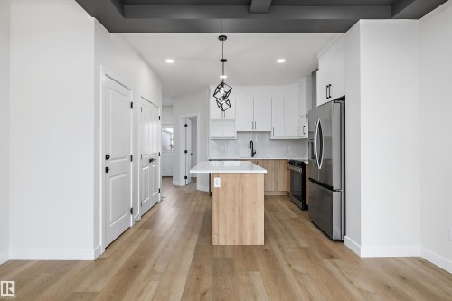 Kitchen featuring wood-finish flooring, white cabinetry, a central island with a white countertop, stainless steel appliances, and a geometric pendant light fixture - 960 Elderberry Landing Nw, Edmonton, AB 