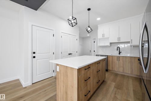 Modern kitchen featuring a central island with a solid surface countertop, wood-finish cabinetry, and contemporary pendant lighting - 960 Elderberry Landing Nw, Edmonton, AB 