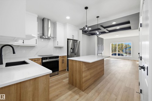 Kitchen with white shaker cabinetry, stainless steel appliances, a center island with white countertops, wood-finish flooring, and a coffered ceiling - 960 Elderberry Landing Nw, Edmonton, AB 