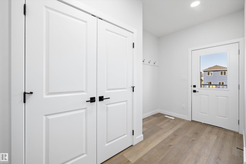 Wood-finish flooring, recessed lighting, white panel doors, matte black hardware, and a glass-paneled exterior door - 960 Elderberry Landing Nw, Edmonton, AB 