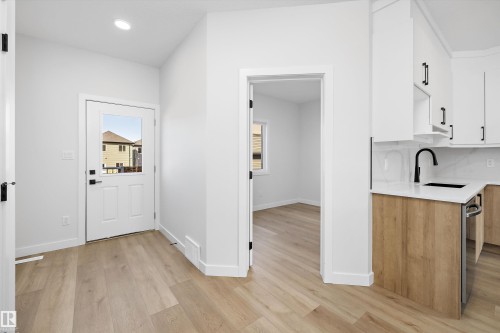 Wood-finish flooring, white cabinetry with matte black hardware, white quartz-finish countertop, and a black gooseneck faucet - 960 Elderberry Landing Nw, Edmonton, AB 