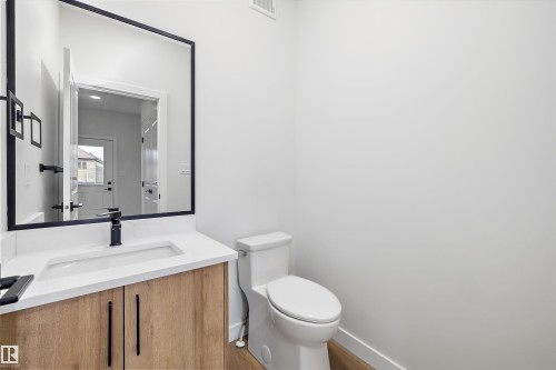 Contemporary vanity with wood-finish cabinetry, white countertop, integrated sink, and matte black hardware - 960 Elderberry Landing Nw, Edmonton, AB 