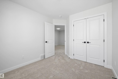 Plush carpet flooring, crisp white walls, white paneled doors, matte black hardware, and overhead lighting - 960 Elderberry Landing Nw, Edmonton, AB 