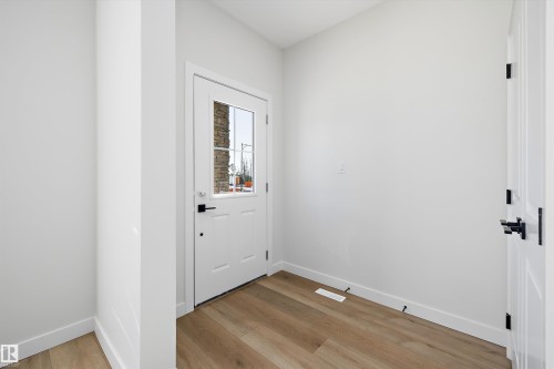 Entryway featuring a white paneled door with window inserts, wood-finish flooring, and crisp white walls - 960 Elderberry Landing Nw, Edmonton, AB 