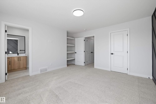Plush carpeting throughout, a round flush-mount ceiling light, built-in shelving, and a panel-style door with dark hardware - 960 Elderberry Landing Nw, Edmonton, AB 