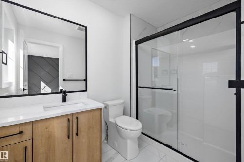 Modern bathroom featuring a wood-finish vanity with a white countertop, rectangular under-mount sink, and matte black fixtures - 960 Elderberry Landing Nw, Edmonton, AB 