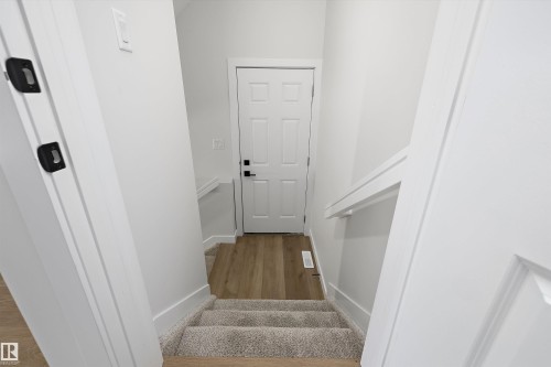 Carpeted stairs leading to a paneled door with black hardware, flanked by white walls and a white handrail - 960 Elderberry Landing Nw, Edmonton, AB 