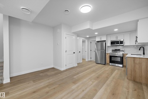 Wood-finish flooring throughout, stainless steel appliances, white cabinetry with modern hardware, light-toned countertops, and recessed lighting fixtures - 960 Elderberry Landing Nw, Edmonton, AB 