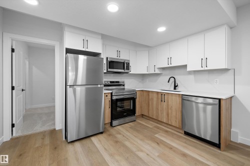 Kitchen featuring stainless steel appliances, white upper cabinetry, wood-finish lower cabinetry, white countertops, and wood-finish flooring - 960 Elderberry Landing Nw, Edmonton, AB 