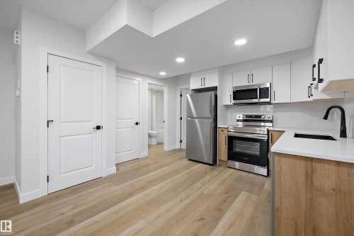 Modern kitchen featuring white cabinetry, stainless steel appliances, wood-finish flooring, white countertops, and a black faucet - 960 Elderberry Landing Nw, Edmonton, AB 