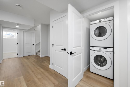 Light wood-finish flooring, white doors with matte black hardware, recessed lighting, and a stacked washer and dryer in a dedicated closet - 960 Elderberry Landing Nw, Edmonton, AB 