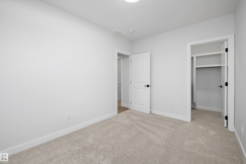 Neutral tone carpeting, white interior doors with black hardware, and an open closet with built-in shelving - 960 Elderberry Landing Nw, Edmonton, AB 