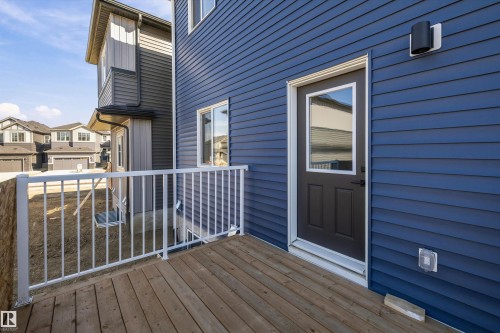 Wood-finish deck with white metal railings, featuring blue horizontal siding and a dark paneled door with an integrated window - 960 Elderberry Landing Nw, Edmonton, AB 