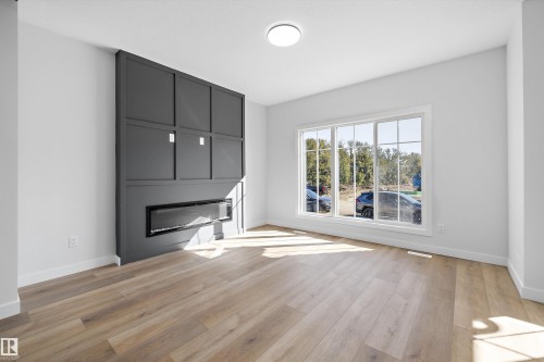 Wood-finish flooring, built-in electric fireplace, contemporary wall paneling, large multi-pane window, and recessed lighting - 960 Elderberry Landing Nw, Edmonton, AB 