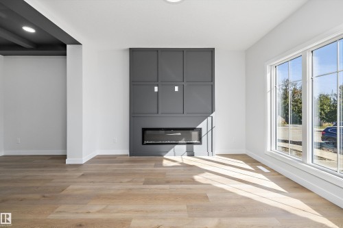 Wood-finish flooring, white walls, large windows, dark accent wall with electric fireplace, and dark exposed ceiling beams - 960 Elderberry Landing Nw, Edmonton, AB 